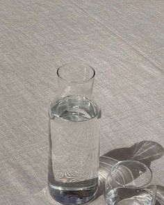 an empty glass with water in it sitting on a tablecloth next to two silver dishes