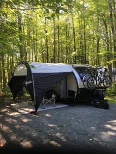 an rv parked in the woods with its awning open and bicycles on it's roof