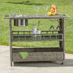 a wicker bar cart with bottles and glasses on it in front of some grass