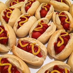 many hotdogs with ketchup and mustard are arranged on a white platter