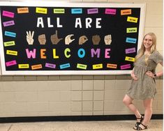 a woman standing in front of a bulletin board that says all are welcome with hand prints on it