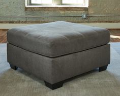 a square footstool sitting on top of a rug in front of a window