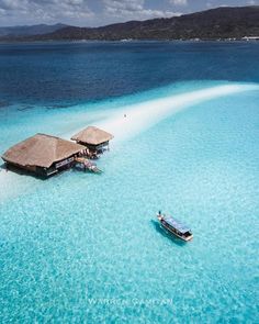 an aerial view of two boats in clear blue water with thatched huts on stilts