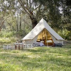 a tent in the middle of a field with tables and chairs around it, surrounded by trees