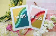 two cards with the words hugs and hello written on them, next to some flowers