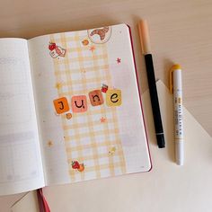 an open notebook sitting on top of a wooden table next to a pen and marker