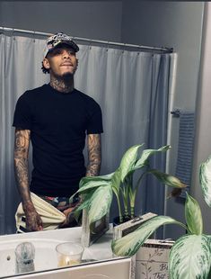 a man with tattoos standing in front of a bathroom mirror next to a potted plant