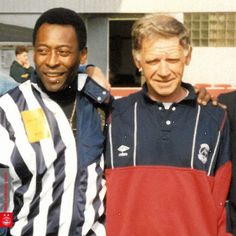 two men standing next to each other in front of a building and one is wearing a referee's shirt