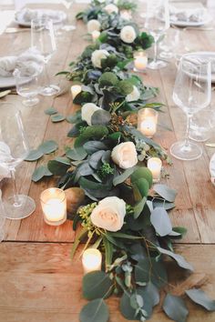 a long table with candles and greenery on the top is decorated with white roses