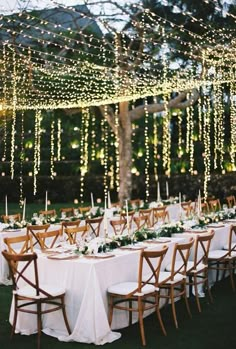 an outdoor dinner table set up with white linens and lights strung from the ceiling