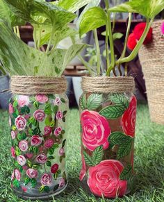 two vases with flowers painted on them sitting in the grass next to some potted plants