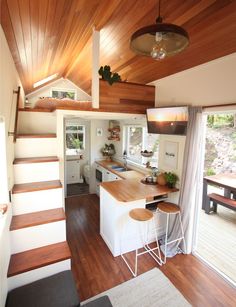 a kitchen and dining area in a tiny home with wood floors, white walls, and stairs leading up to the upper floor