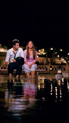 a man and woman sitting next to each other on a bench in the rain at night