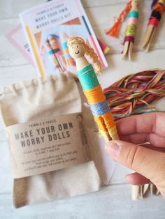 a hand holding a doll made out of yarn next to other crafting supplies on a table