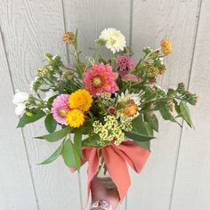 a person holding a bouquet of flowers in front of a white wooden wall with a pink ribbon