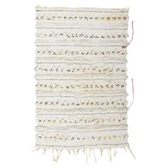 a white rug with fringes and beads on the edges, against a white background