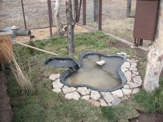 a small pond in the middle of a yard with rocks around it and a fence behind it