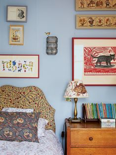 a bedroom with blue walls and pictures on the wall above the bed, along with a wooden dresser