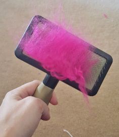 a hand holding a pink brush with purple powder on it