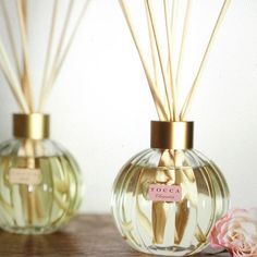 two bottles with reeds in them sitting on a table next to a pink flower