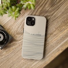 an iphone case sitting on top of a wooden table next to a camera and plant