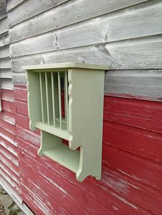 a red and white house with a green shelf on it's side, next to a brick wall