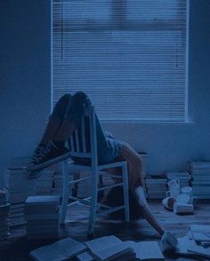 a person sitting in a chair with their head on a stack of books next to a window