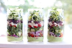 three mason jars filled with different types of salads and veggies, sitting on a window sill