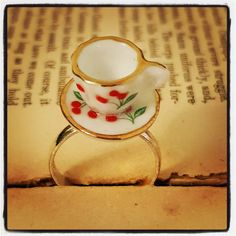 a white and gold ring with cherries on it sitting on top of an open book