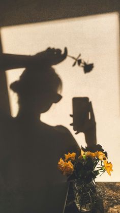 the shadow of a person with a hat and flowers in a vase