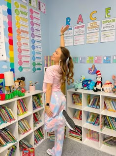 a girl in pink shirt and tie dye leggings standing next to bookshelves