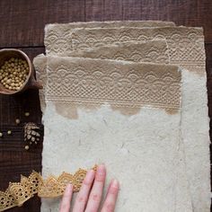 a person is working on some paper with lace and beads next to other items that are sitting on the table