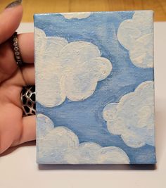 a hand holding a small square painted with white clouds and leopard print on blue background