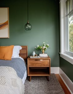 a bedroom with green walls and a wooden nightstand next to a bed in front of a window