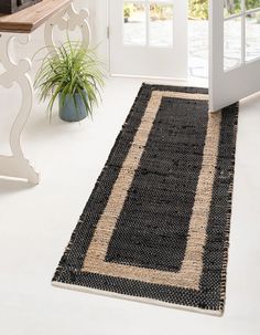 a black and tan rug on the floor in front of a door with a potted plant next to it