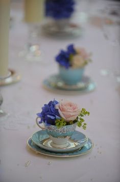 the table is set with tea cups and saucers filled with flowers, candles and napkins