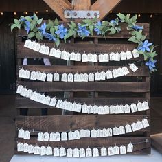 a wooden pallet with seating cards attached to it and flowers on the top shelf