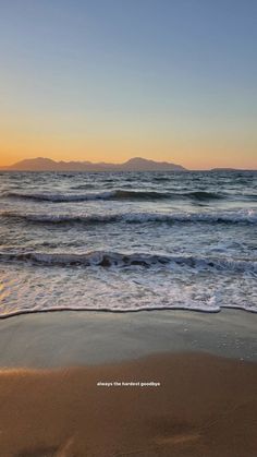 an image of the beach with waves coming in from the water and mountains in the distance