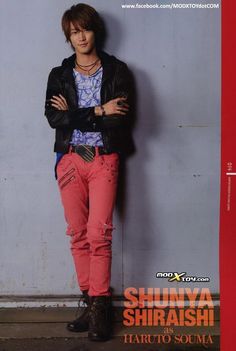 a young man standing in front of a wall wearing pink pants and a black jacket