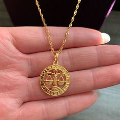 a person is holding a gold necklace with an image of the zodiac sign on it