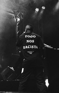 a man standing on top of a stage with his back turned to the camera while wearing a shirt that says fogo nos racism