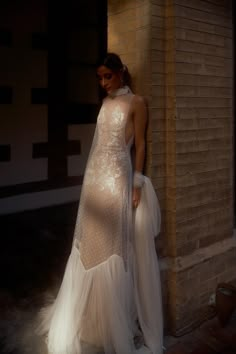 a woman standing in front of a brick wall wearing a white dress with sheer sleeves