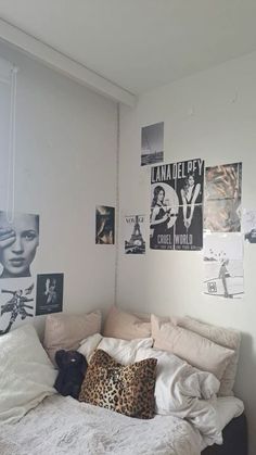 an unmade bed in a small room with posters on the wall and pictures above it