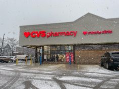 a cv's pharmacy store with snow falling on the ground and cars parked outside