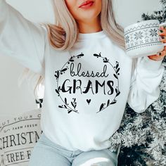 a woman holding a coffee mug in front of a christmas tree wearing a white sweatshirt