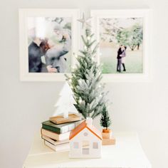 a small christmas tree sitting on top of a white table next to two framed pictures