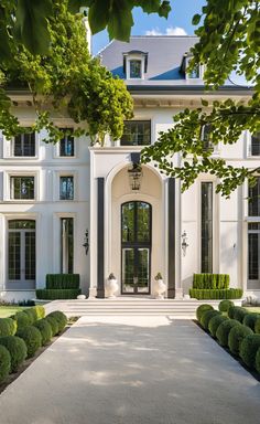 a large white house with lots of windows and bushes in front of the entrance to it