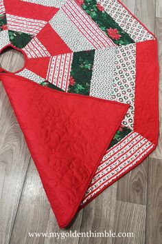 a quilted table runner with red and green christmas decorations on the top, sitting on a wood floor