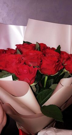 a bouquet of red roses is wrapped in white paper and being held by someone's hand