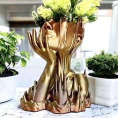 a gold sculpture with flowers in it on a table next to some potted plants